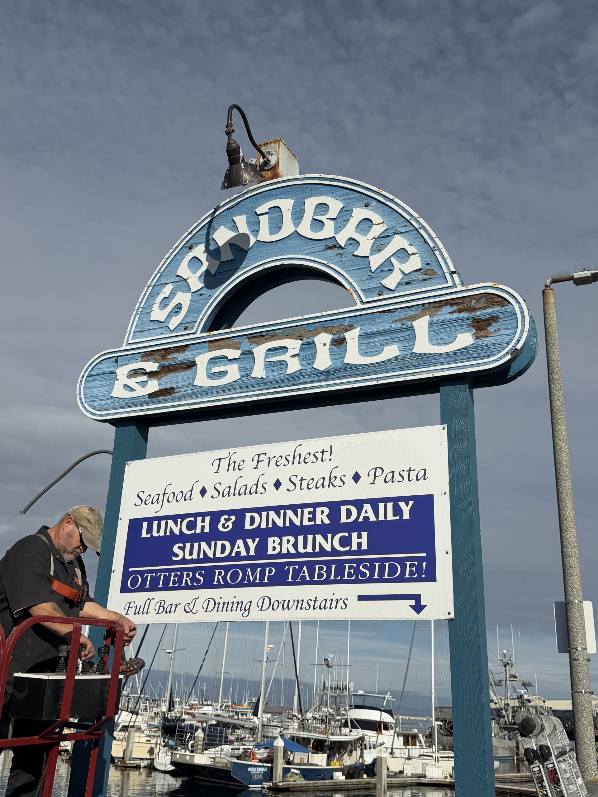 Old deteriorating Sandbar and Grill sandblasted sign on Municipal Wharf 2 Monterey showing peeling paint and crumbling wood