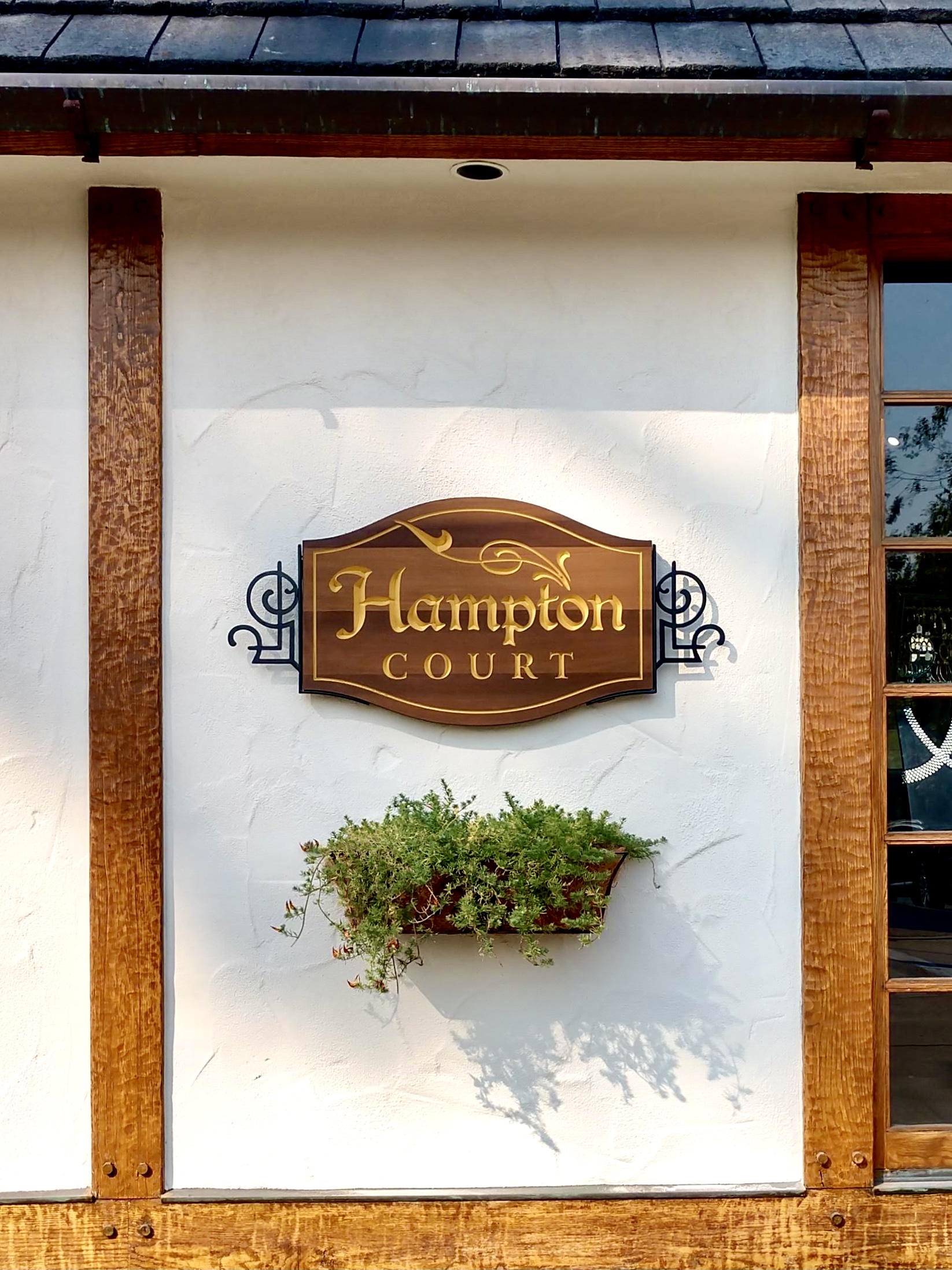 Hampton Court wall sign in context with Carmel cottage architecture — stucco walls, exposed wood beams, and slate roof