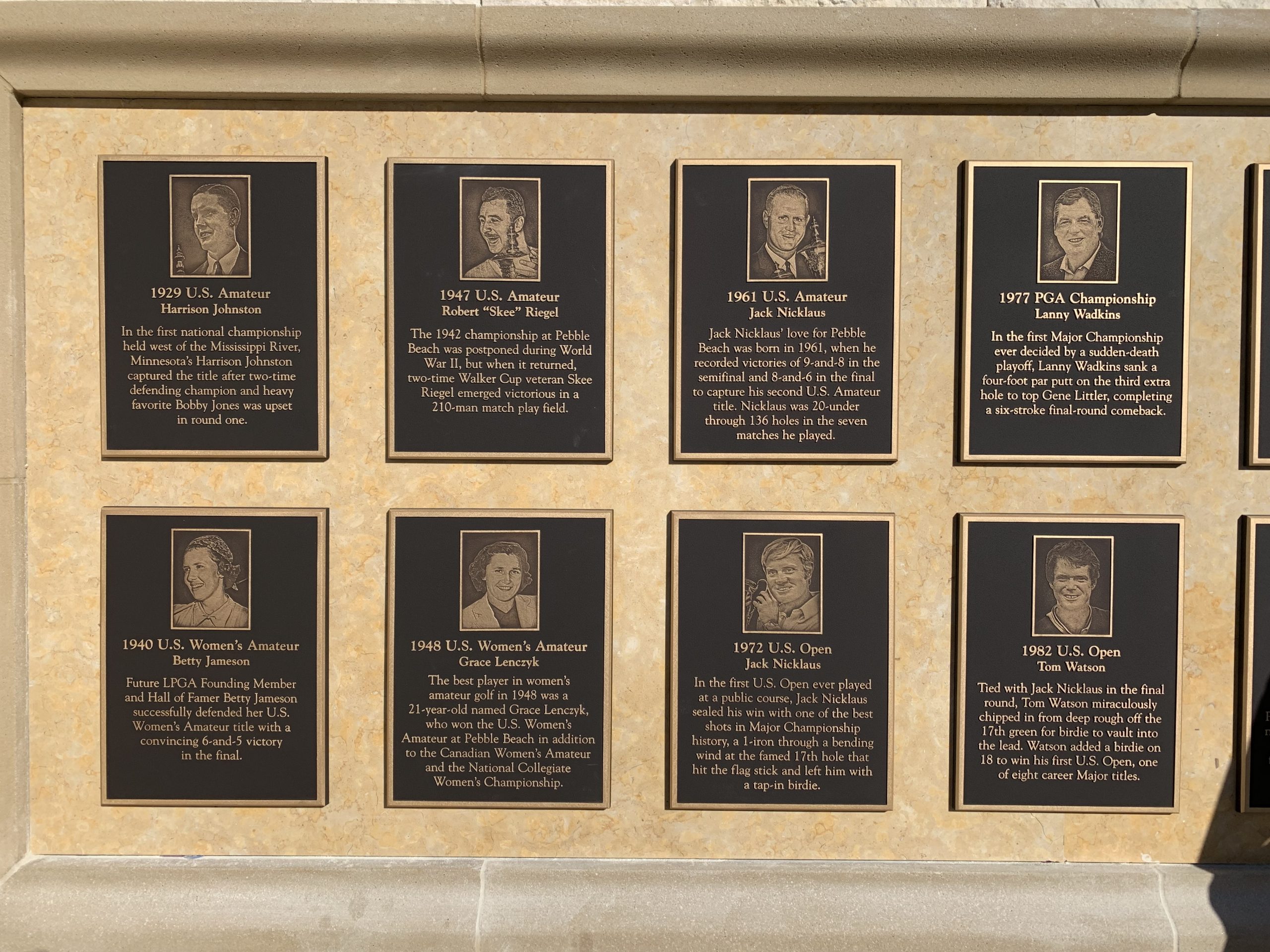 Close-up of individual cast bronze champion plaques at Pebble Beach showing photographic bronze portraits and raised text