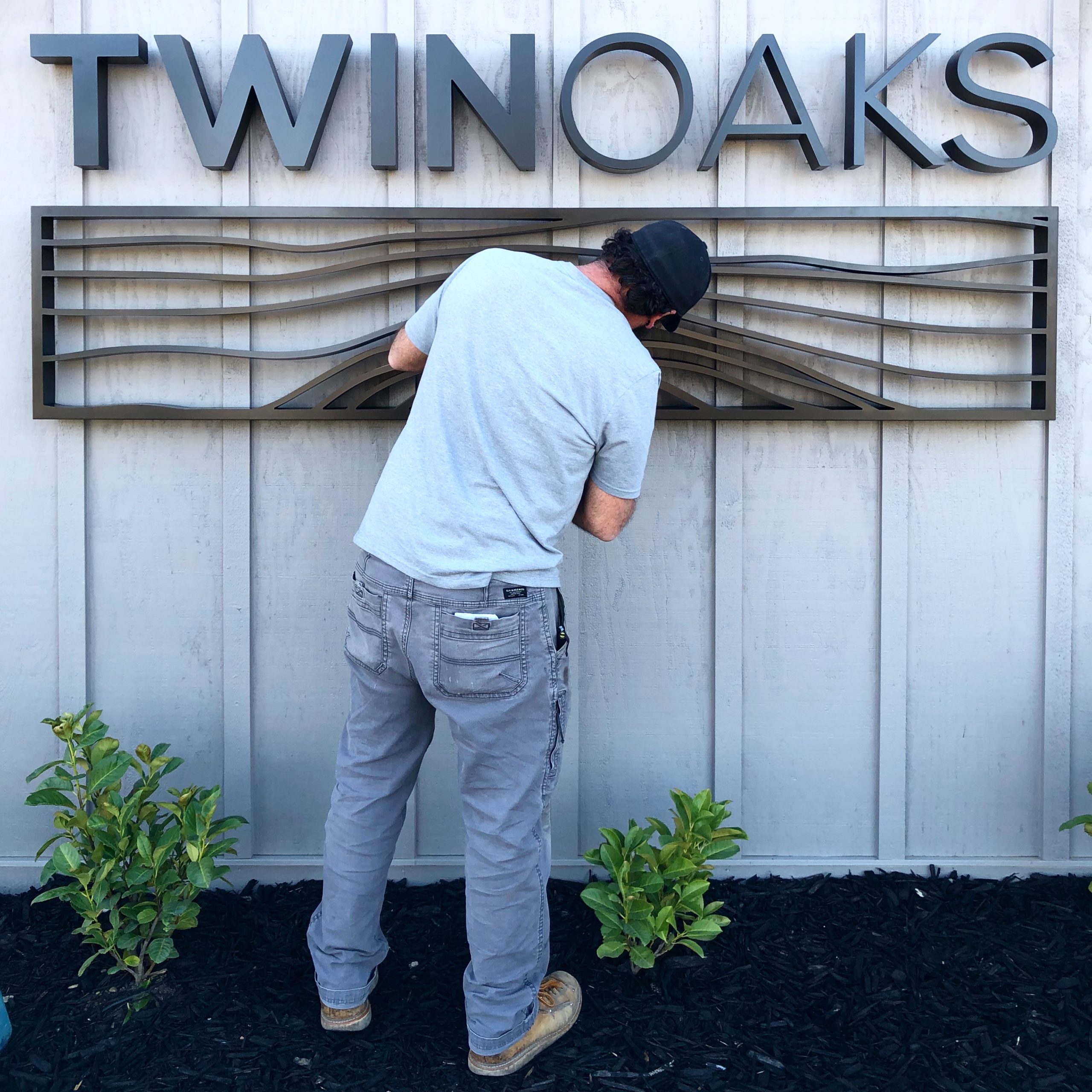 Signworks installer mounting Twin Oaks dimensional letters and bronze wave art