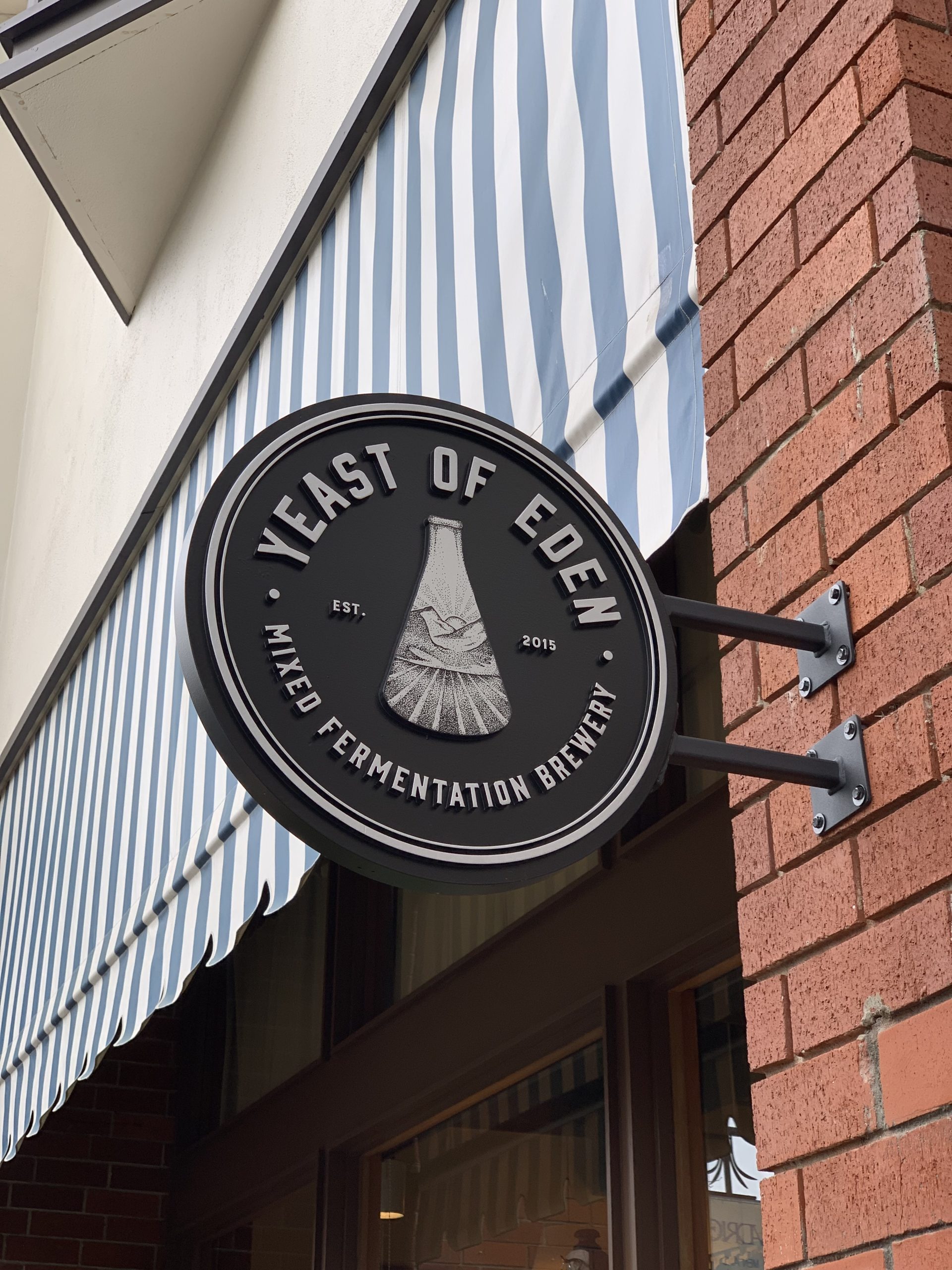 Yeast of Eden circular projecting blade sign on brick building in Carmel