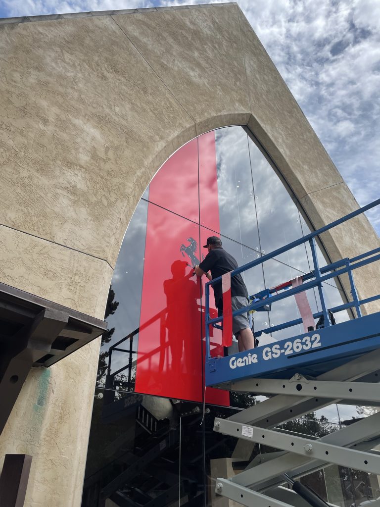 Signworks installer applying large red vinyl building wrap on venue facade for corporate event